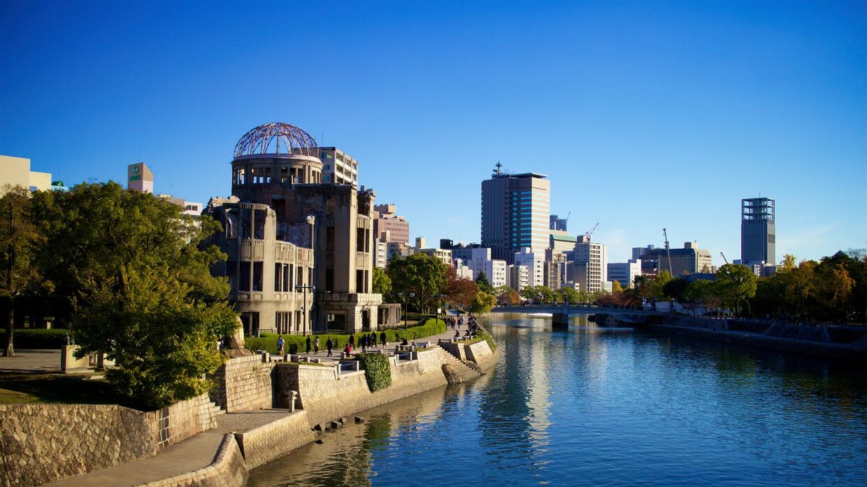 Hiroshima Peace Memorial (A-Bomb Dome) beside river with modern city skyline and blue sky in background