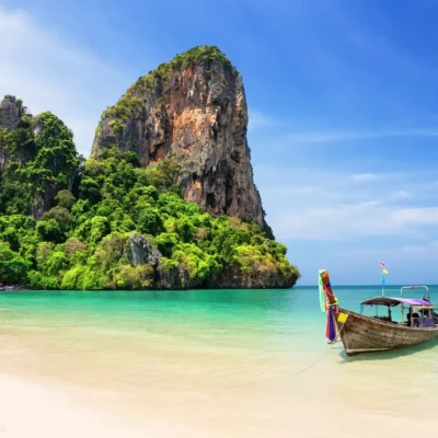 Traditional longtail boat on turquoise waters at Thai beach with dramatic limestone cliffs and lush tropical vegetation