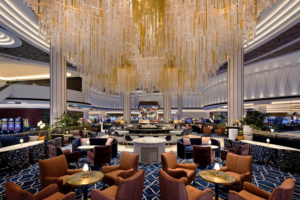 Luxurious casino lounge with dramatic golden chandelier, orange leather seating, and gaming floor in upscale hotel