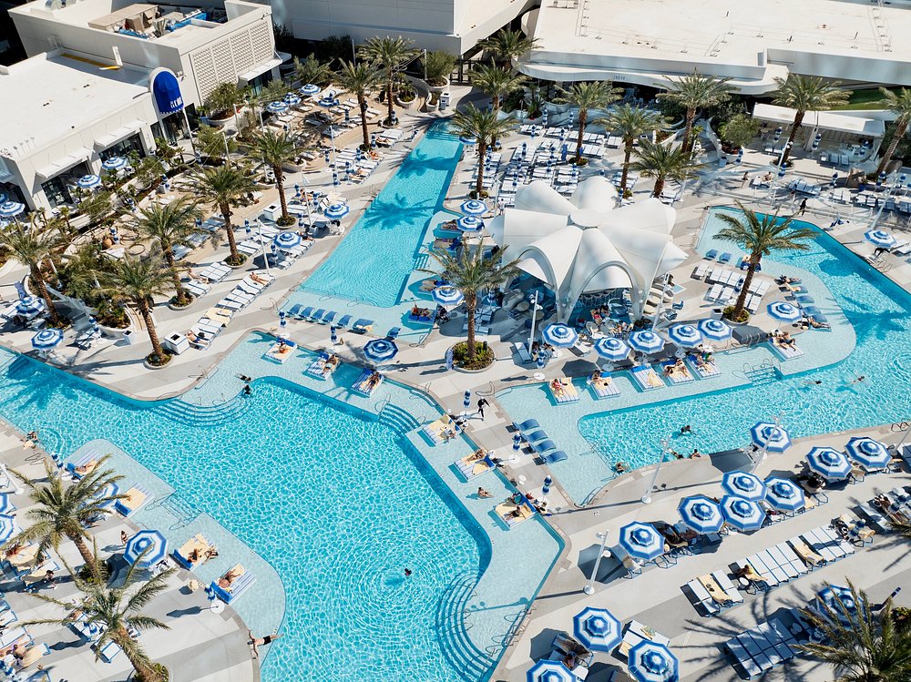 Aerial view of Fontainebleau Las Vegas resort pool area with blue striped umbrellas, palm trees, and multiple swimming pools