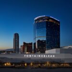 Fontainebleau hotel and casino building lit up at dusk in Las Vegas, with curved glass tower and illuminated signage against blue sky