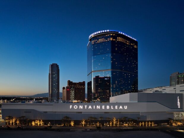 Fontainebleau hotel and casino building lit up at dusk in Las Vegas, with curved glass tower and illuminated signage against blue sky