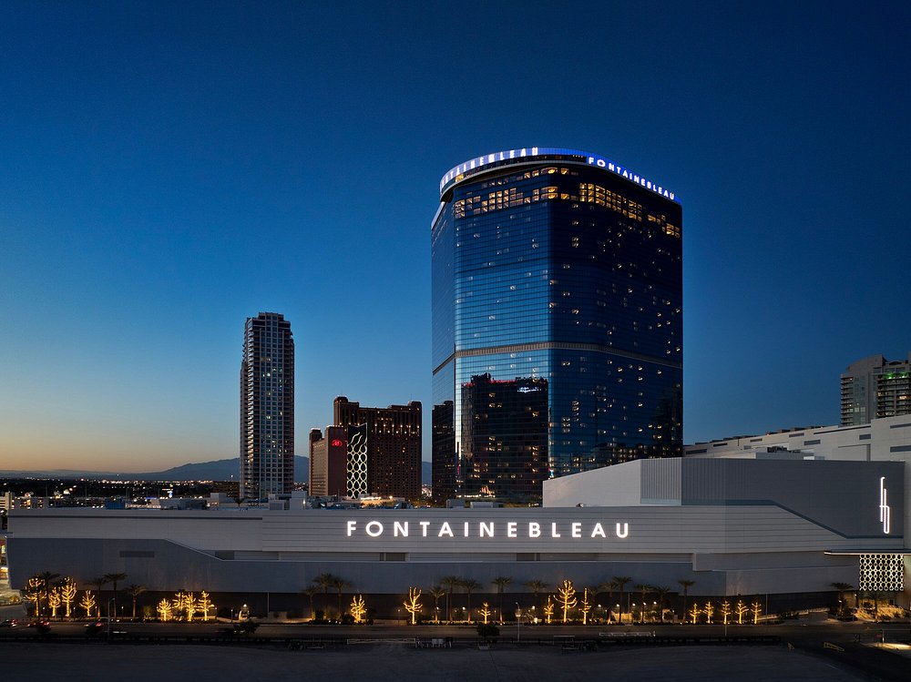Fontainebleau hotel and casino building lit up at dusk in Las Vegas, with curved glass tower and illuminated signage against blue sky